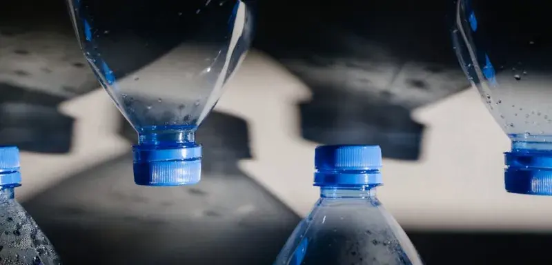 Gros plan sur des bouteilles en plastique avec bouchons bleus projetant des ombres, illustrant les enjeux du recyclage