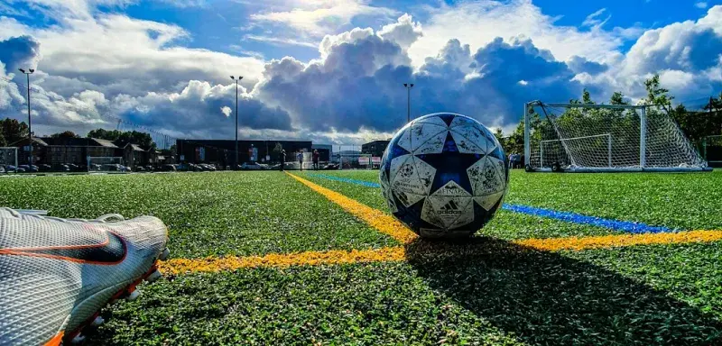 Ballon de football bleu et gris sur un terrain vert sous un ciel nuageux