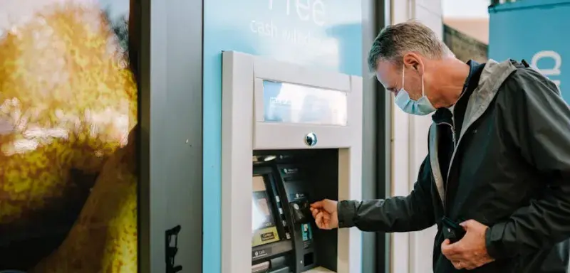 Un homme portant un masque utilise un distributeur automatique de billets en extérieur