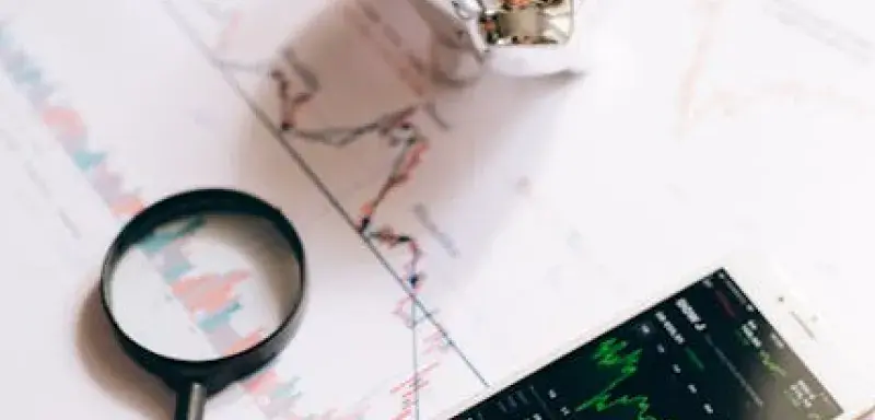 Un smartphone affichant des graphiques boursiers, une tirelire et une loupe sur des documents financiers