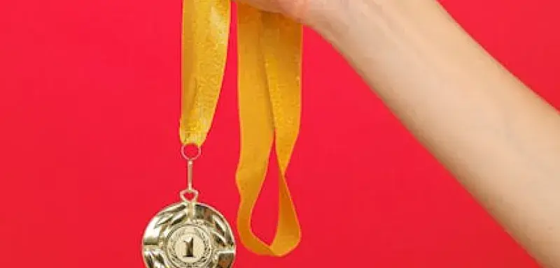 Une main tenant une médaille d'or avec un ruban jaune sur fond rouge vif, symbole de victoire olympique