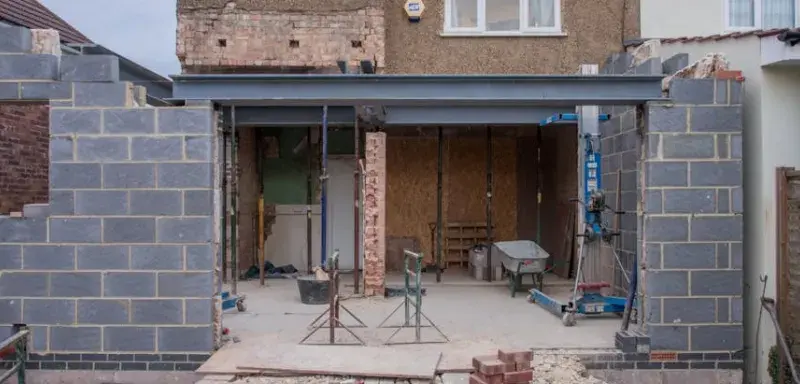 Maison en briques en cours de rénovation avec une extension visible et des matériaux de construction sur le chantier