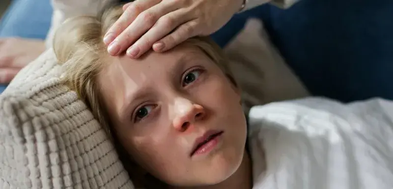 Enfant allongé avec une main vérifiant la fièvre, symbolisant la maladie et les arrêts de travail