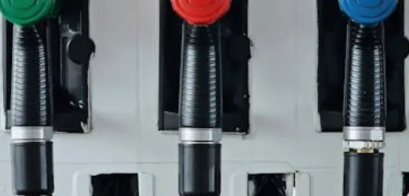 Gros plan sur des poignées de pompes à essence vertes, rouges et bleues dans une station-service