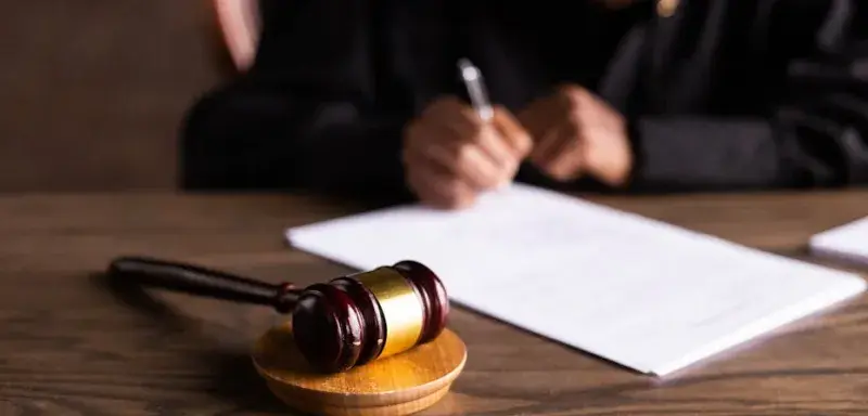Juge signant des documents au bureau, marteau au premier plan, illustrant la justice.