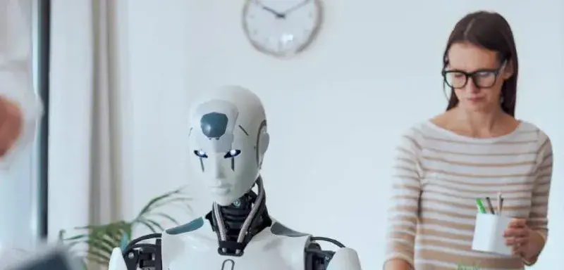 Robot humanoïde dans un bureau aux côtés d'une employée, symbole de l'impact de l'IA sur le travail