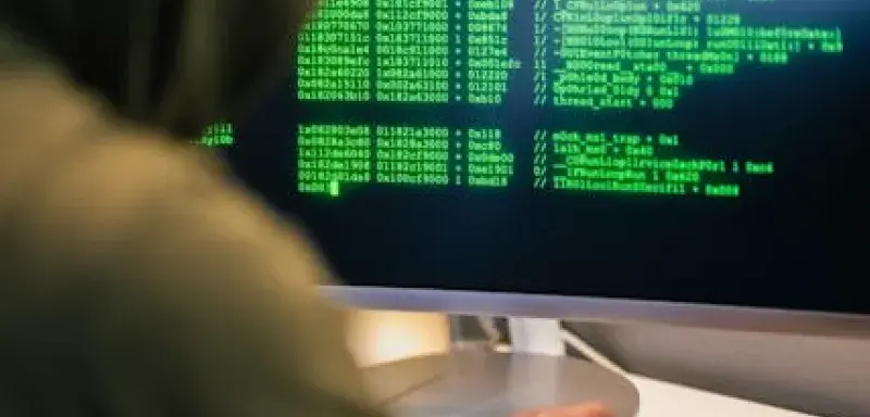 Personne en sweat à capuche tapant du code sur un écran d'ordinateur, représentant une scène de piratage informatique
