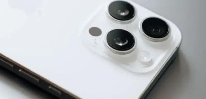 White smartphone with triple cameras lies atop a sleek laptop.