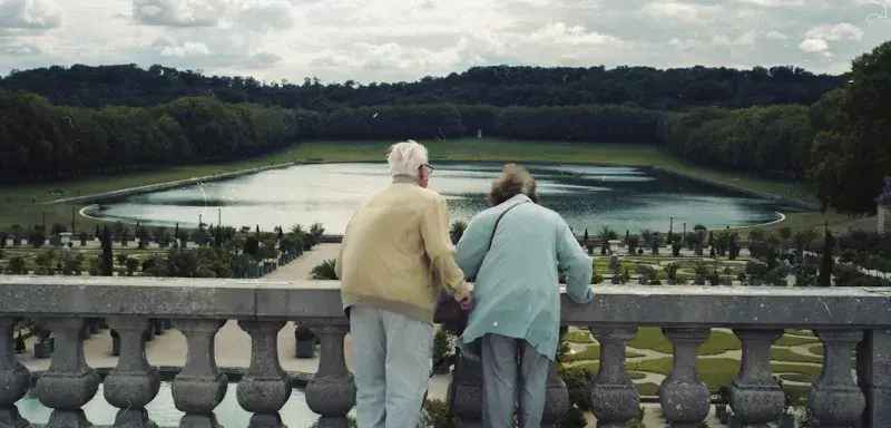 Elderly couple holding hands overlooking a formal garden.
