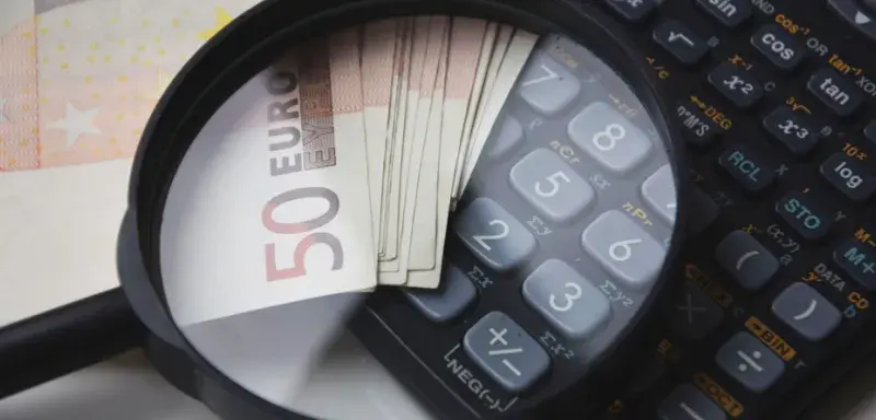 Euro bills under magnifying glass with calculator, symbolizing finance and analysis.