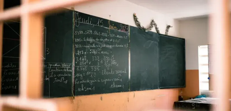 A classroom with a blackboard displaying mathematical equations in French, seen through a window.