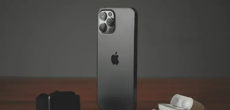 A smartphone, a smartwatch, and wireless earbuds on a wooden surface