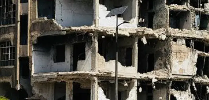 Desolate war-damaged building in Homs, Syria, with a truck in foreground.