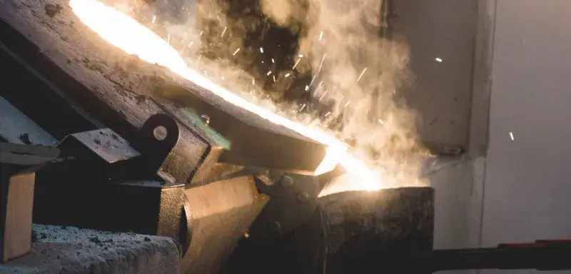 Molten metal being poured in an industrial setting, showcasing intense heat and light.