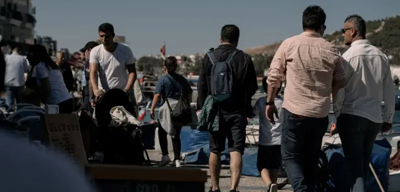 People walking through a busy street market under bright summer sunlight.