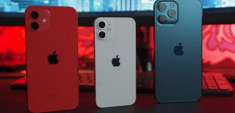 Three smartphones in red, white, and blue on a desk with a computer monitor