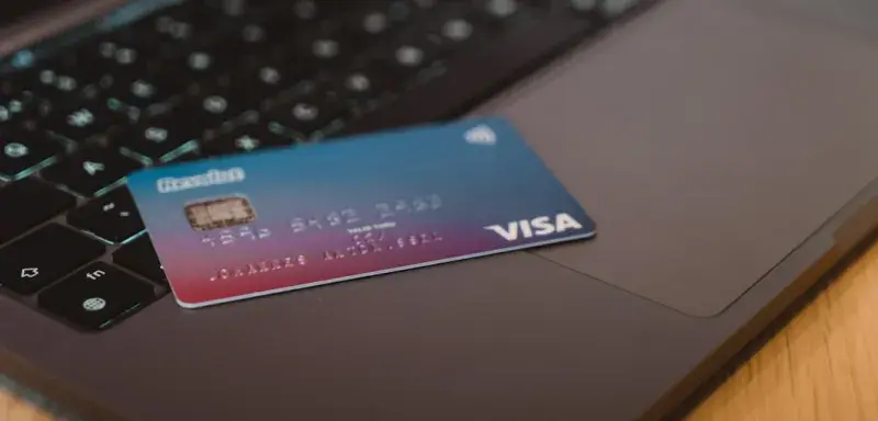 A blue and red gradient debit card resting on a dark laptop keyboard