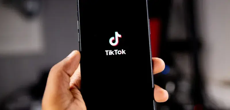 Une main tenant un smartphone affichant le logo TikTok sur fond noir