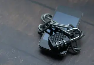 Close-up of a smartphone wrapped in a chain with a padlock, symbolizing strong security.