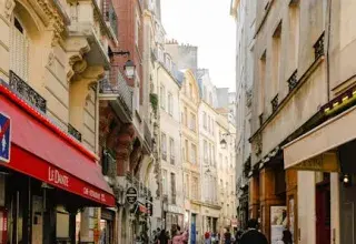 Rue parisienne typique bordée d'immeubles historiques et de commerces, illustrant le cadre urbain de la capitale