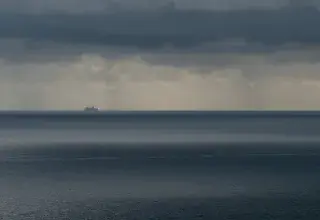 Un navire solitaire navigue sous des nuages orageux sur une mer vaste et menaçante