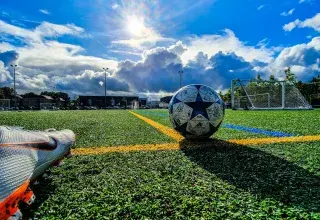 Ballon de football bleu et gris sur un terrain vert sous un ciel nuageux