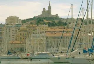 Capture of Marseille's Old Port with yachts and distant view of Notre-Dame de la Garde on a sunny day.