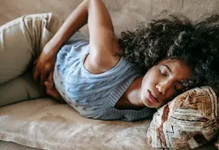 Femme afro-américaine allongée sur un canapé, les yeux fermés, souffrant de douleurs menstruelles