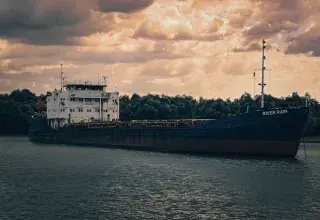 Navire cargo naviguant sur une rivière sous un ciel nuageux