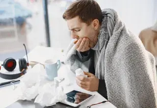 Homme enveloppé dans une couverture, se sentant malade à la maison, entouré de mouchoirs et de médicaments