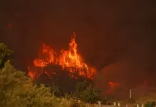 A dramatic wildfire consuming a forest area with intense flames and heavy smoke.
