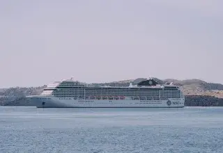 White MSC cruise ship sailing peacefully on the sea against a scenic coastline backdrop.