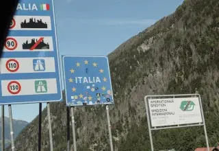 Road signs for italy and eu at a mountain border.