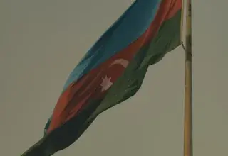 The Azerbaijani national flag waving on a flagpole against a clear sky, symbolizing national pride.