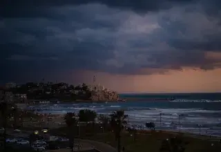 a storm rolls in over the ocean with a city in the distance
