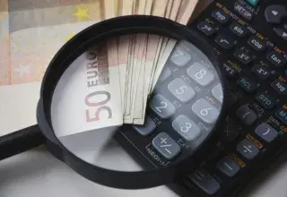 Euro bills under magnifying glass with calculator, symbolizing finance and analysis.