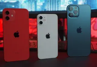 Three smartphones in red, white, and blue on a desk with a computer monitor