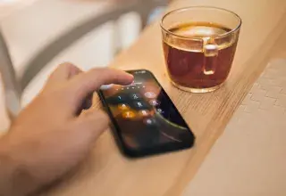 Main saisissant un code sur l'écran de verrouillage d'un smartphone posé à côté d'une tasse de thé
