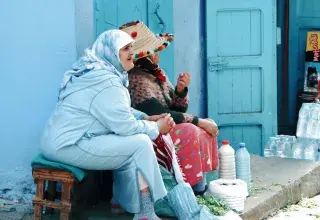 Deux femmes discutent devant une échoppe aux murs bleus dans une médina du Maroc