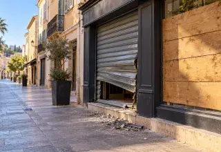 Illustration générée : boutique au rideau forcé et vitrine protégée par des planches dans une rue du sud de la France.